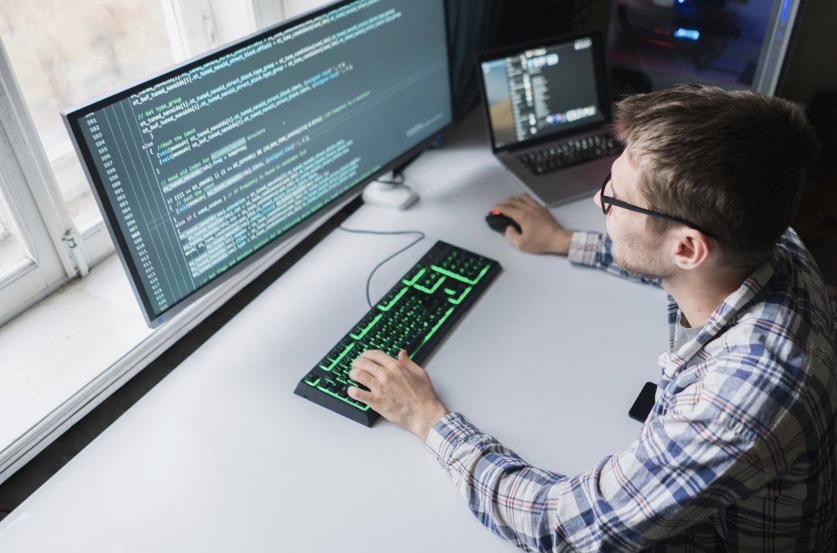 Bespectacled man sat coding on a computer