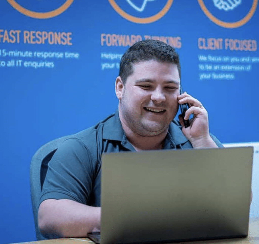 Smiling Your IT Department staff member on the phone, and working on his laptop